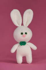 Amigurumi rabbit doll on pink background. Front view. Concept symbol of Catholic Easter. White Easter bunny crocheted, handmade art.