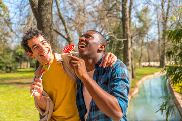 Couple of multi ethnic men eating a lollipop, lgbt concept, having fun and smiling