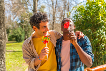 Obraz premium Couple of multi ethnic men eating a lollipop, lgbt concept, having fun and smiling