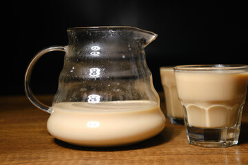 Coffee with milk in coffee pot and two thin espresso cups on wooden background