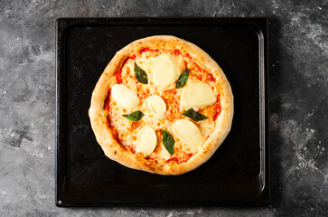 Frozen Italian Pizza Margherita with Mozzarella and Basil Leaves on Dark Background