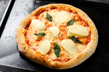Frozen Italian Pizza Margherita with Mozzarella and Basil Leaves on Dark Background