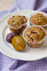 Seasonal muffins with plums and poppy seeds on white wooden and textile background close up selective focus 