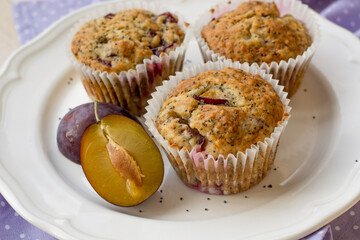 Seasonal muffins with plums and poppy seeds on white wooden and textile background close up selective focus 