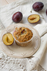 Seasonal muffins with plums and poppy seeds on white wooden and textile background close up selective focus 