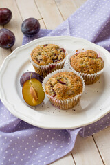 Seasonal muffins with plums and poppy seeds on white wooden and textile background close up selective focus 
