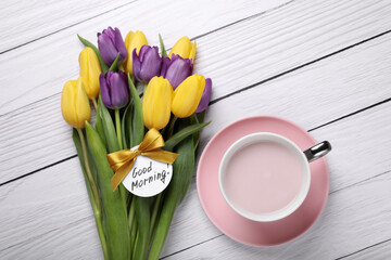 Cup of hot drink, beautiful tulips and card with text Good Morning on white wooden table, flat lay