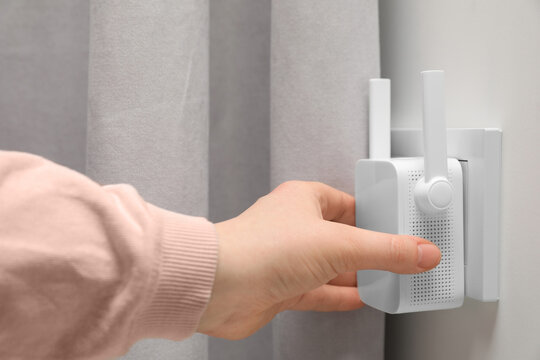 Woman turning on wireless Wi-Fi repeater indoors, closeup