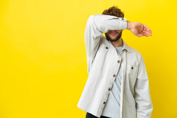 Young handsome caucasian man isolated on yellow background covering eyes by hands