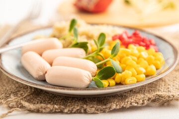 Mixed quinoa porridge, sweet corn and small sausages on white wooden, side view, selective focus.