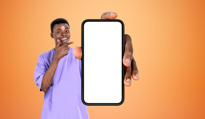 Naklejka na ściany i meble Black man pointing at big phone empty screen, bright background