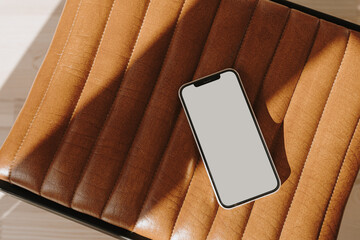 Flatlay mobile phone on orange leather bench with sunlight shadows. Aesthetic elegant blog, online...