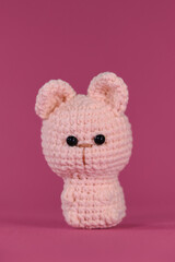 Amigurumi one little cute kitten sitting on pink background. Soft DIY toy made of natural cotton and wool. Crocheted cat, handmade art. Front view.