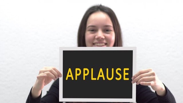 Conceptual message "Applause" on canvas frame label hold by beautiful girl smiling at camera