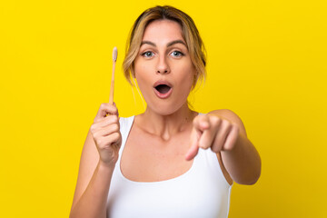 Young Uruguayan woman brushing teeth isolated on yellow background surprised and pointing front