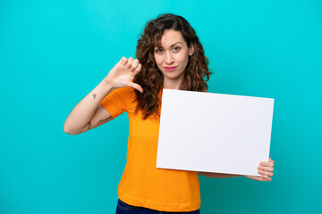 Young caucasian woman isolated on blue background holding an empty placard and doing bad signal