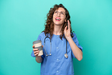 Young nurse caucasian woman isolated on blue background holding coffee to take away and a mobile