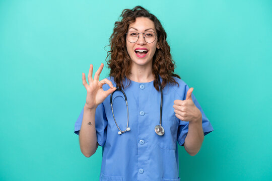 Young nurse caucasian woman isolated on blue background showing ok sign and thumb up gesture