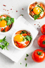 Baked Eggs with Bacon, Tomatoes, Spinach and Herbs on Bright Background, Healthy Breakfast or Snack