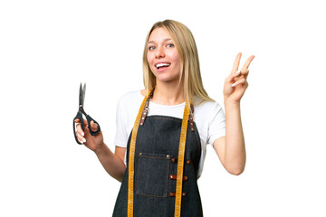 Young blonde Seamstress woman over isolated chroma key background smiling and showing victory sign