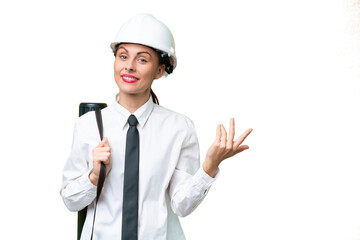 Young architect woman with helmet and holding blueprints over isolated background extending hands to the side for inviting to come
