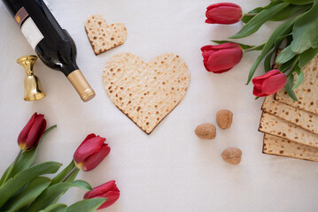 Matzah shape of hearts with red tulips, kosher wine and walnut on white background. Passover celebration concept. Traditional ritual Jewish bread, Passover food. Pesach Jewish holiday.