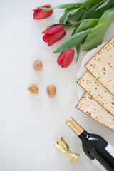 Matzah on white plate with red tulips, bottle of wine and walnut on white background. Traditional Holiday on Passover. Home symbol of lovely Jewish family in pesach. top view