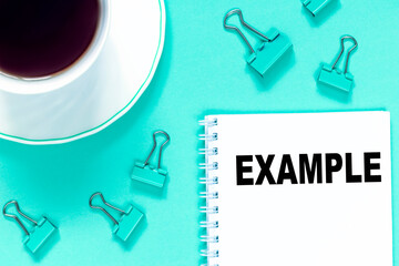 The word EXAMPLE is written in the notebook with office tools and cup of coffe. Business concept