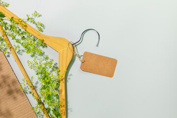 Sustainable, ecological shopping, buying or sales concept. Eco friendly still life with wooden hanger with green branches and empty label on blue background with plant shadows. Flat lay, copy space