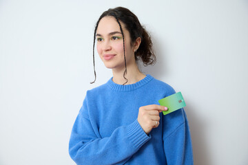 Cheerful young curly haired woman with small braids make-up smiling and looking away while holding a credit card in her hand. Happy woman recommending electronic banking and online shopping.