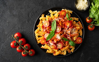 Fusilli pasta with tomatoes, basil, parmesan, and sauce on back background