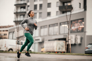 A fast urban female runner is running on the rainy day downtown.