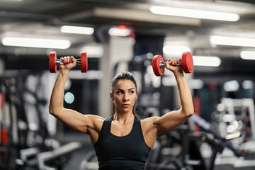 Portrait of a strong muscular female bodybuilder lifting dumbbells in a gym.