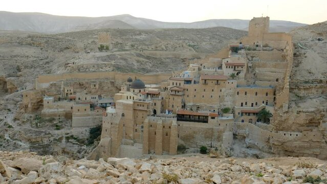 A fantastic wide shot of a Byzantine period monastery, built on the rocks above a desert wadi. an evening 4K video clip. Mar Saba, the holy land.