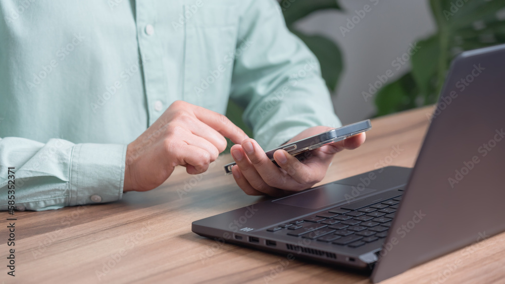 Poster Male hand using a smartphone while working on computer laptop at office for investment analyzing company financial report balance with mobile phone. Concept of people are working with mobile devices.