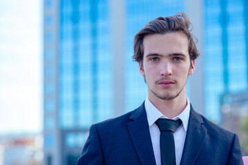 Confident businessman near a business center. A young businessman in a suit outside a tradecenter. A young businessman near a modern tall glass building.