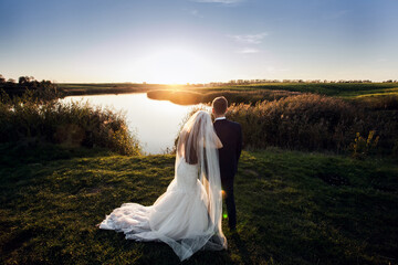 The bride and groom are standing on the shore of the lake at sunset. Image for your creative design or illustrations.