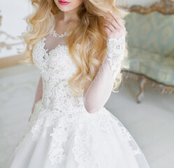 Fototapeta premium A beautiful bride in a white wedding dress, with bright makeup, stands in a room with a stylish interior. Image for your creative design or illustrations.