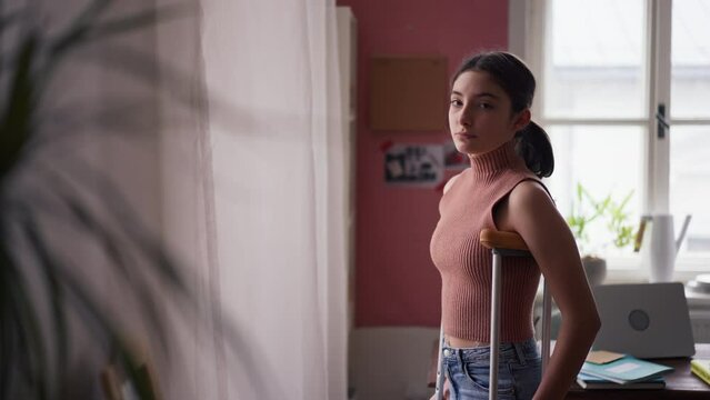 Unhappy girl with broken leg in her room looking trough window