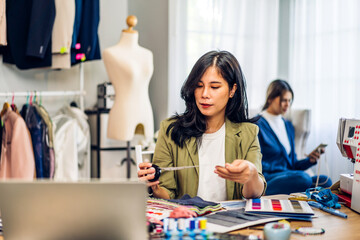 Fototapeta premium Portrait of young beautiful asian woman fashion designer stylish sitting and working with color samples.Attractive young asian girl working with colorful fabrics at fashion studio