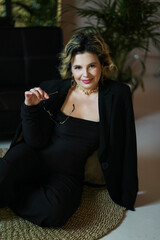 Fototapeta premium A smiling woman in a black suit sits holding glasses.