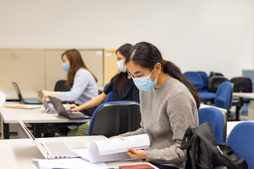 group of happy young boys and girls with face mask work, discuss, study on assignment and teaching materials together in classroom in university in Hong Kong during covid-19