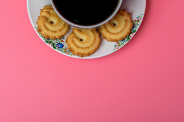 Filiżanka z czarną mocną herbata z ciasteczkami na spodku na różowym tle