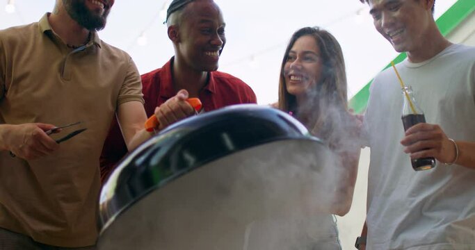 smiling positive friends laughing trying to cook raw burger in bbq grill outdoor.Group of asian,caucasian young men women standing around bbq grill, having fun enjoying weekend together.camera motion