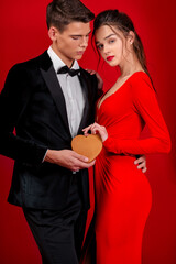 Young lady in the long red dress holding the men's hand wich is wearing black costume. Valentine. People inlove. Lovely caucasian couple together