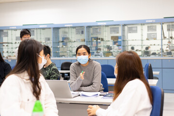 group of happy young boys and girls with face mask work, discuss, study on assignment and teaching materials together in classroom in university in Hong Kong during covid-19