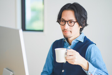 コーヒーを飲みながらリモートワークをする若い男性