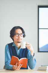 自宅の書斎でコーヒーを飲みながら本を読む若い男性