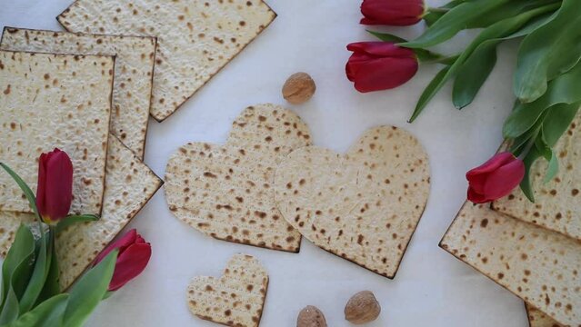 Matzah shape of heart with red tulips, bottle of wine and walnut on white background. Traditional Holiday on Passover. Home symbol of lovely Jewish family in pesach. top view