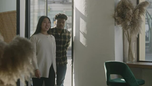 Multi ethnic couple coming to cafe and smiling. Female waiter greets man and woman at entrance and sits people at the table. Diverse guests in restaurant with modern design. Concept of public eating.